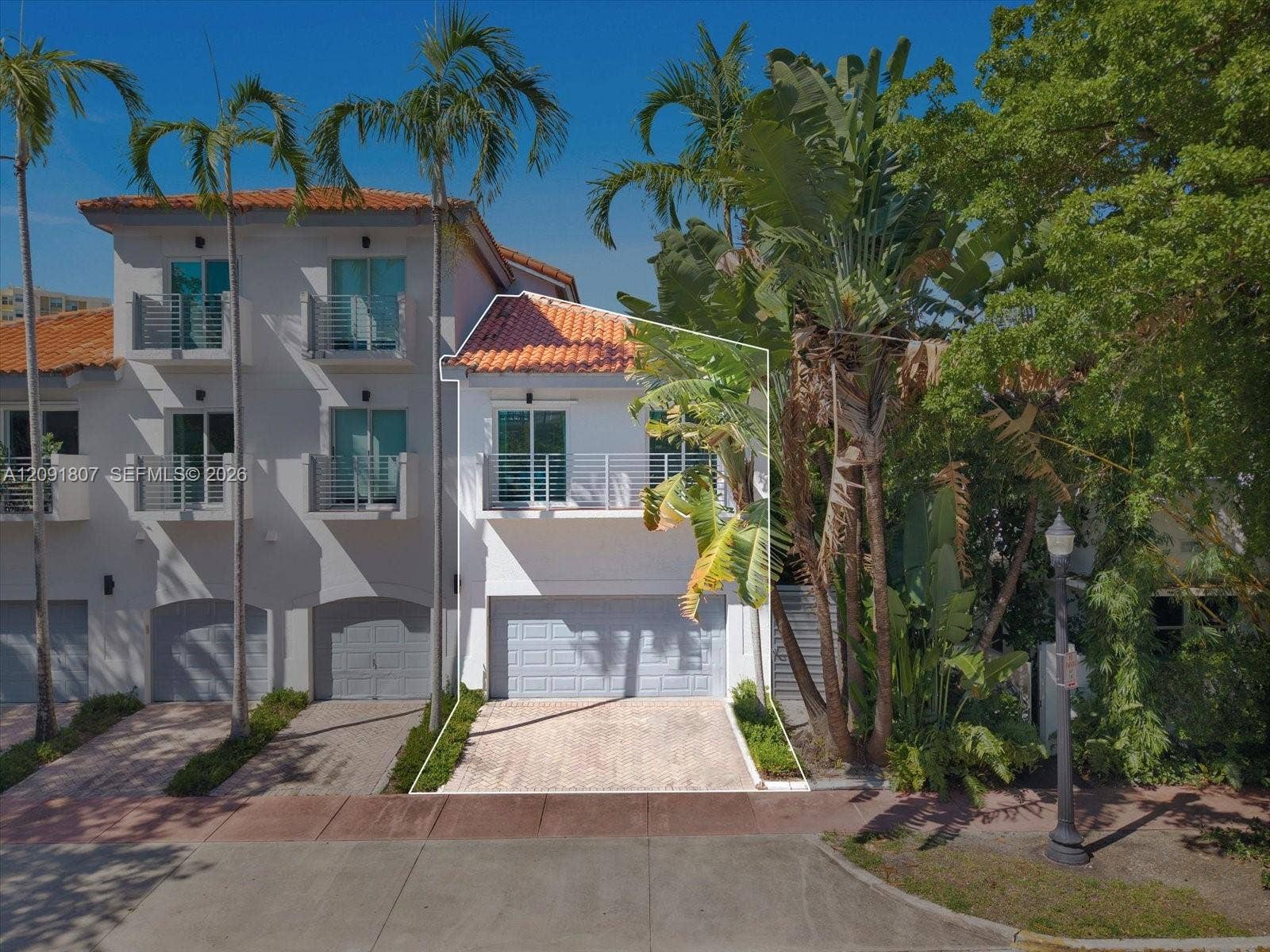 Multi-level exterior featuring a barrel tile roof, private balcony with metal railings, paver driveway, and an attached two-car garage