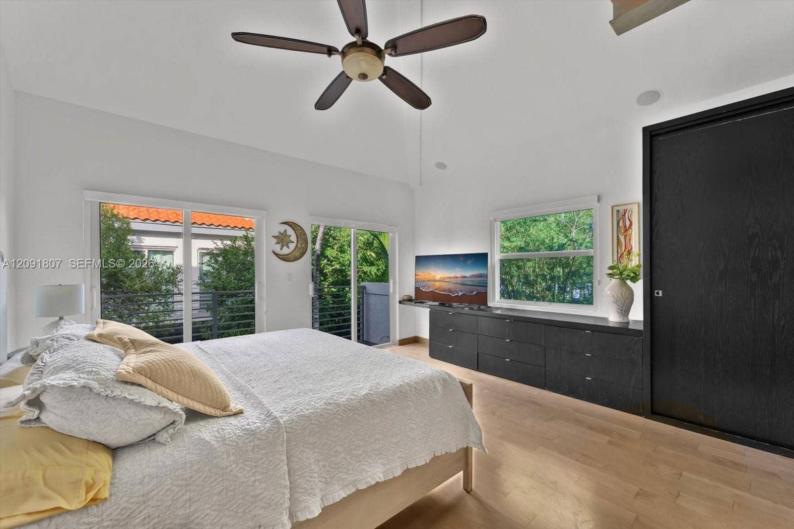 Vaulted ceilings, wood-finish flooring, built-in black cabinetry, ceiling fan, and sliding glass doors