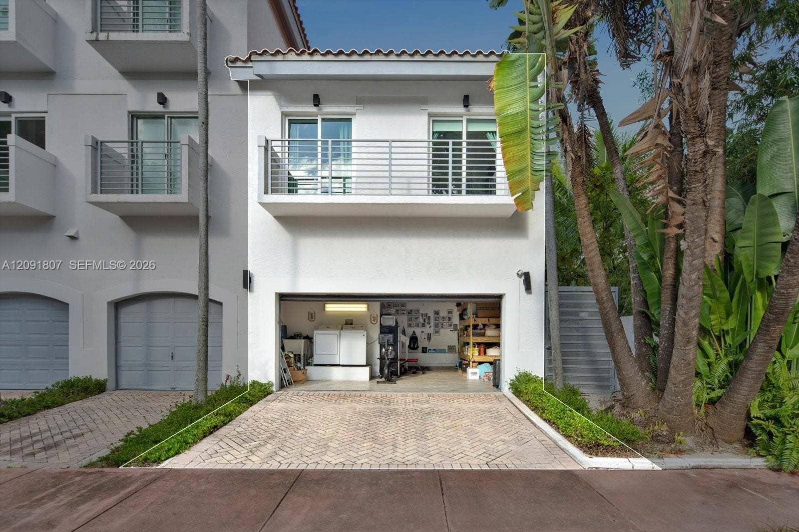 Stucco exterior featuring a second-story balcony with metal railing, a paved driveway, and an attached multi-purpose garage
