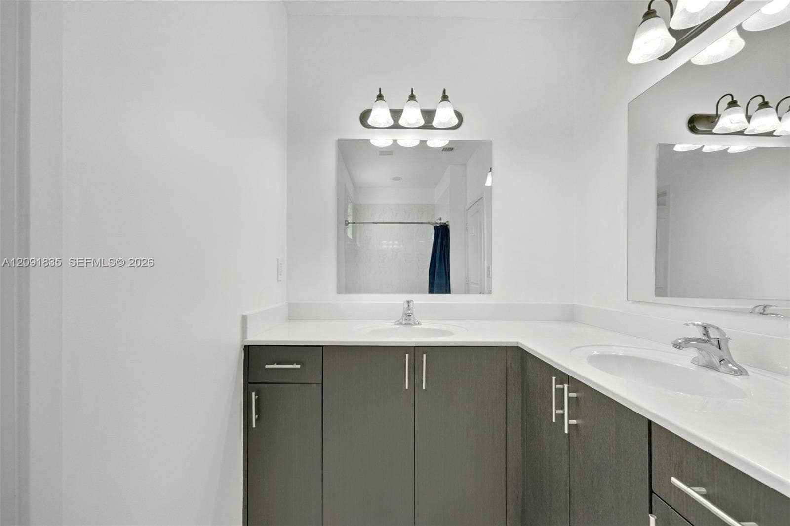 22409 SW 102nd Avenue, Miami, FL 33190 Dual-sink vanity featuring charcoal-toned cabinetry, light-colored solid surface countertops, integrated sinks, polished chrome fixtures, and wall-mounted vanity lighting