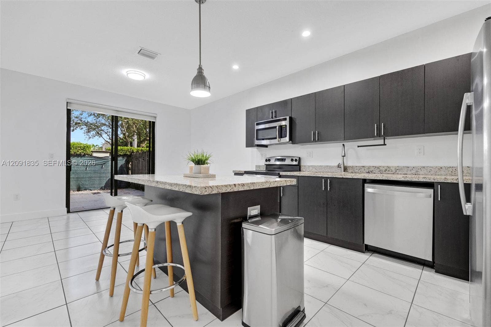 22409 SW 102nd Avenue, Miami, FL 33190 Kitchen featuring dark-toned flat-panel cabinetry, stone countertops, stainless steel appliances, a center island, and large-format tile flooring