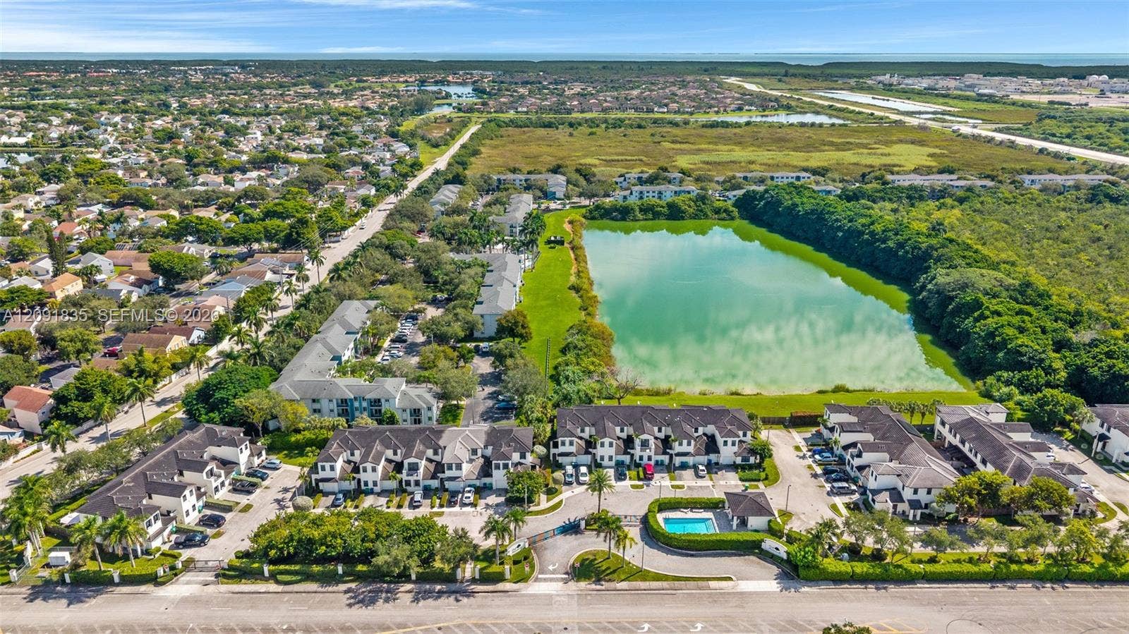 22409 SW 102nd Avenue, Miami, FL 33190 Aerial perspective of a multi-unit residential community featuring a dedicated swimming pool, paved parking, and direct frontage on a natural lake