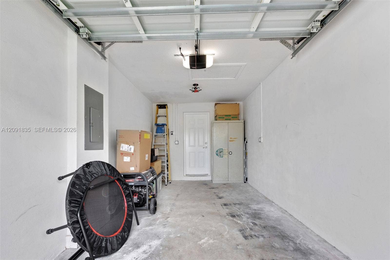 22409 SW 102nd Avenue, Miami, FL 33190 Garage interior featuring a concrete floor, automated overhead door system, ceiling-mounted lighting, integrated electrical panel, and a paneled service door