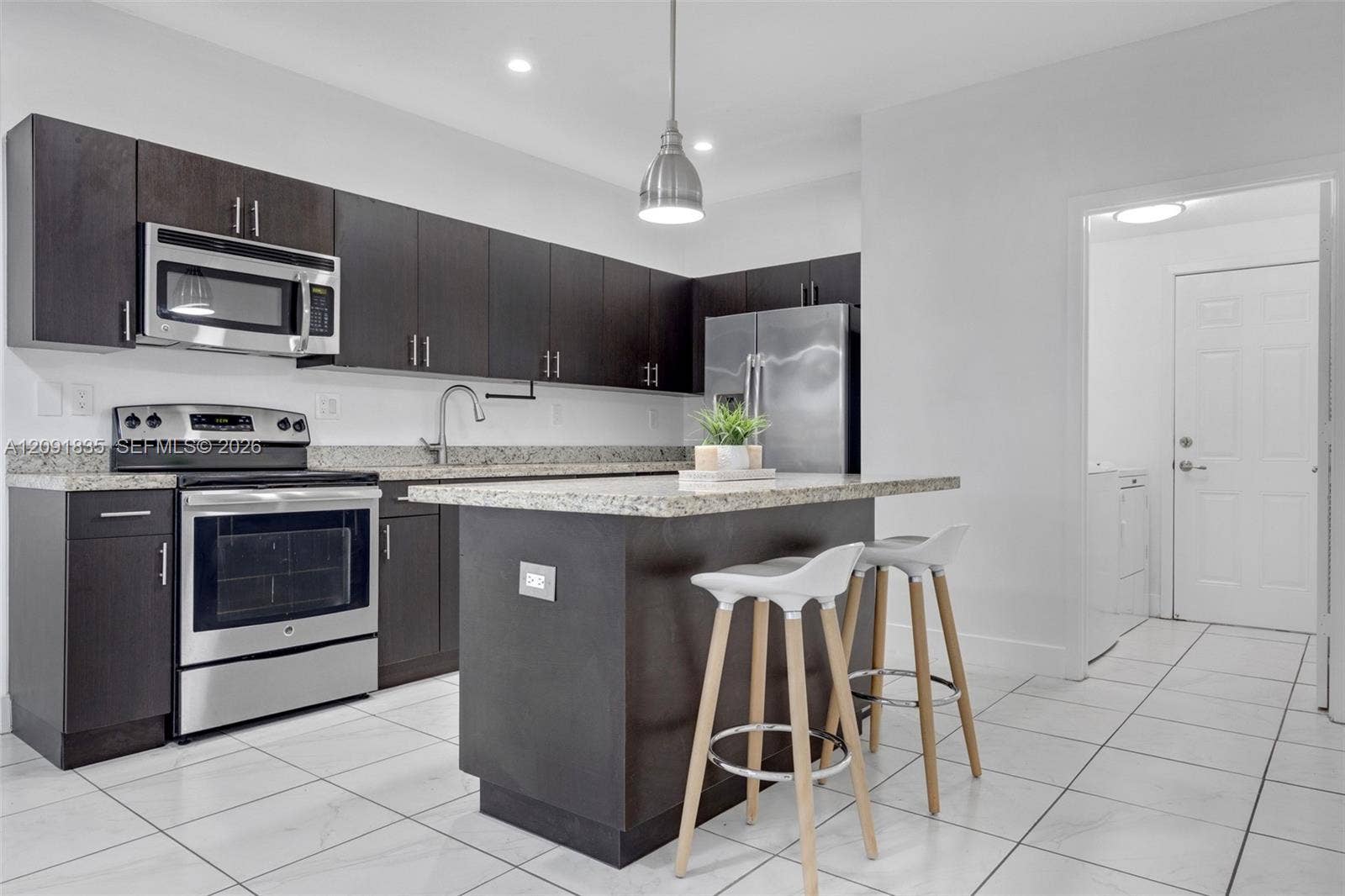22409 SW 102nd Avenue, Miami, FL 33190 Kitchen featuring dark-finish cabinetry, stone-style countertops, stainless steel appliances, a central island, and ceramic tile flooring