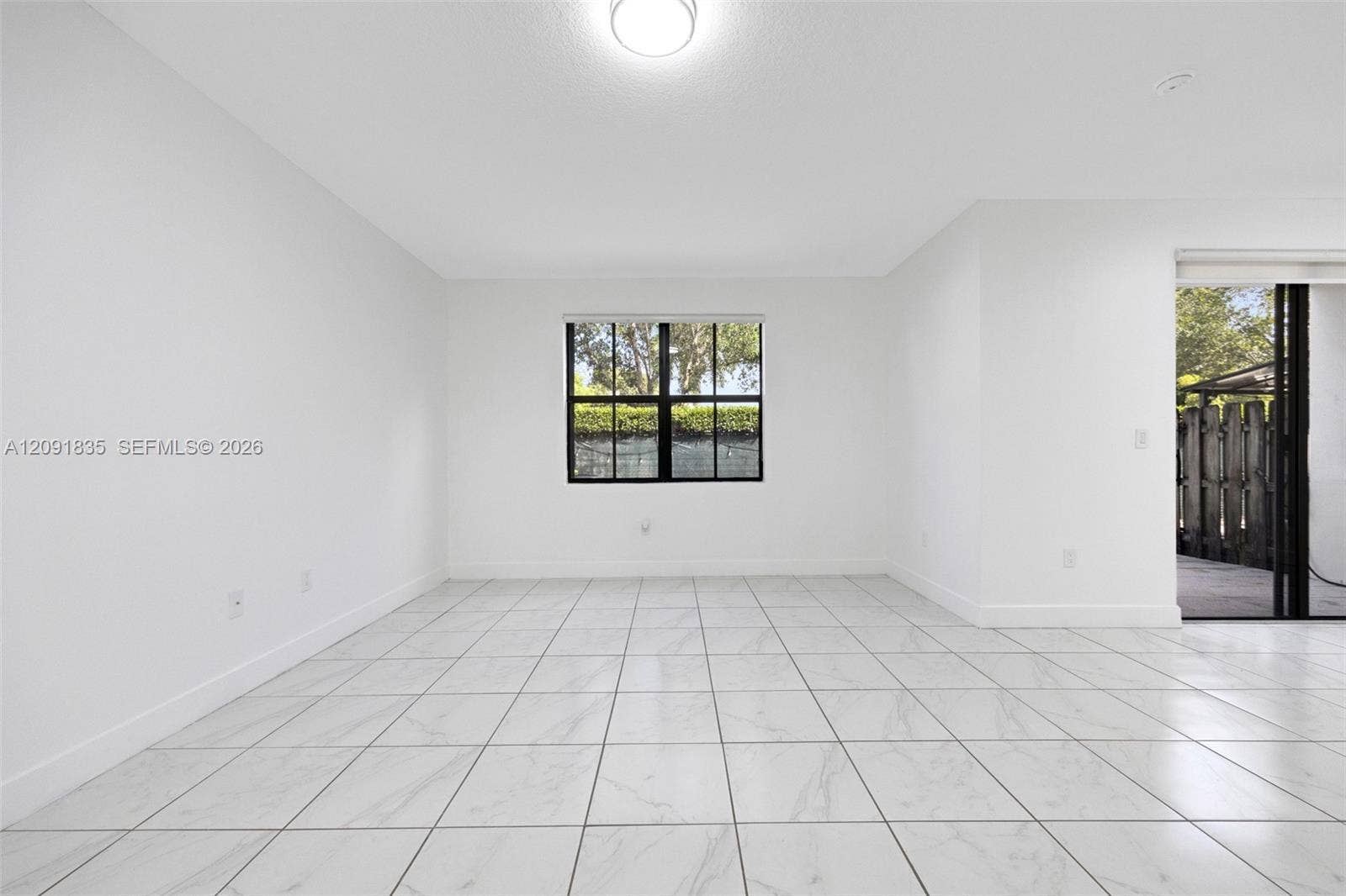 22409 SW 102nd Avenue, Miami, FL 33190 Interior space featuring large-format tile flooring, a centered window with black-framed panes, neutral walls, and sliding glass patio doors