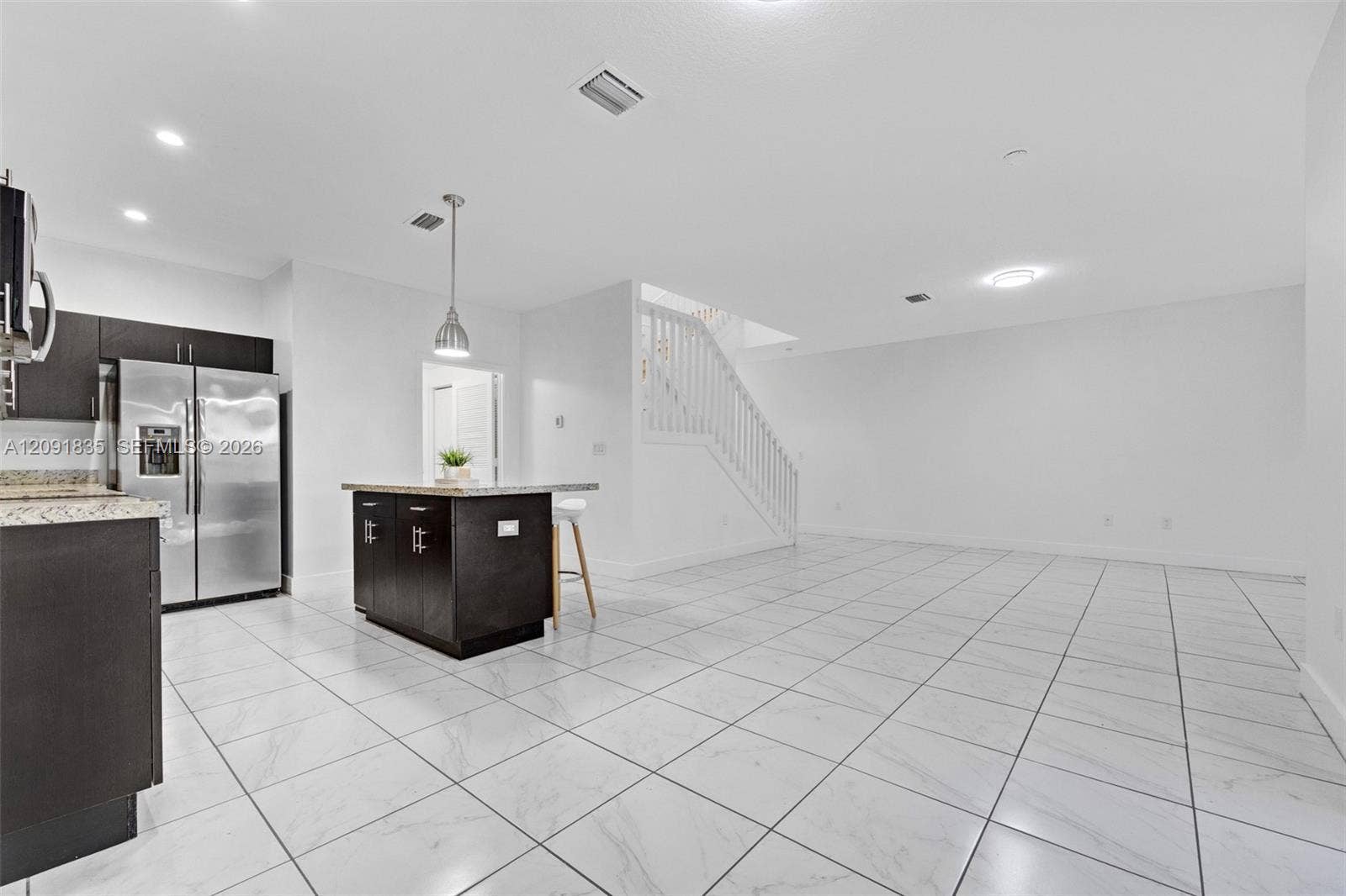 22409 SW 102nd Avenue, Miami, FL 33190 Open-concept area featuring white tile flooring, dark wood-finish cabinetry, stone countertops, a center island with pendant lighting, and a white staircase with wooden balusters