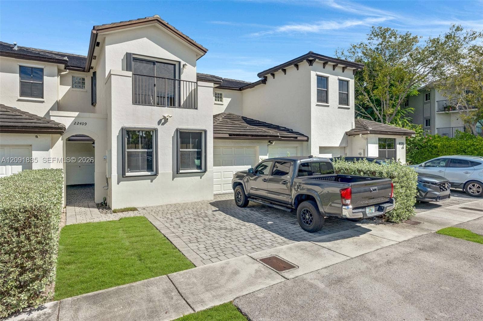 22409 SW 102nd Avenue, Miami, FL 33190 Two-story stucco exterior featuring a tiled roof, upper-level balcony with metal railing, paver driveway, and an integrated garage