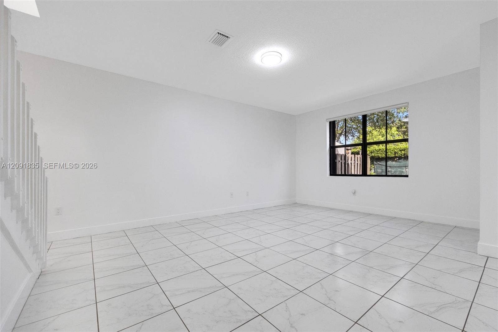 22409 SW 102nd Avenue, Miami, FL 33190 Bright room featuring tile flooring with stone-pattern detail, neutral wall finishes, a multi-pane window with dark trim, and white-painted staircase balusters