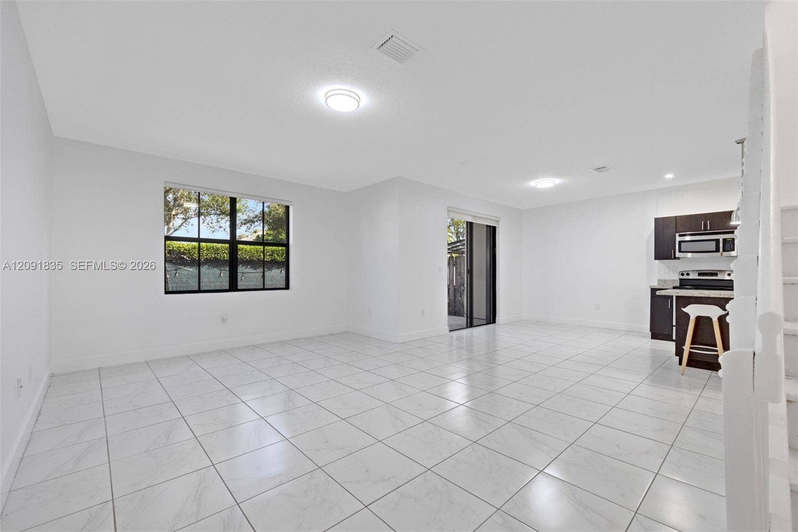 22409 SW 102nd Avenue, Miami, FL 33190 Open-concept interior featuring large-format tile flooring, recessed lighting, expansive windows with dark frames, and kitchen cabinetry with integrated stainless steel appliances