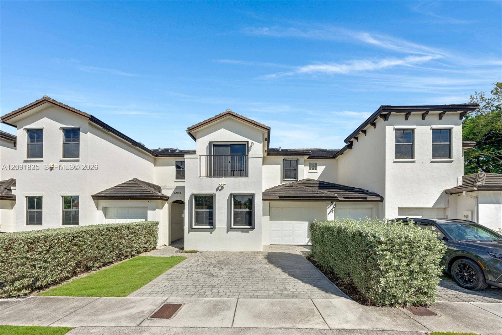 22409 SW 102nd Avenue, Miami, FL 33190 Stucco exterior featuring multiple attached garage bays, a paved driveway, and an upper-level balcony with metal railings