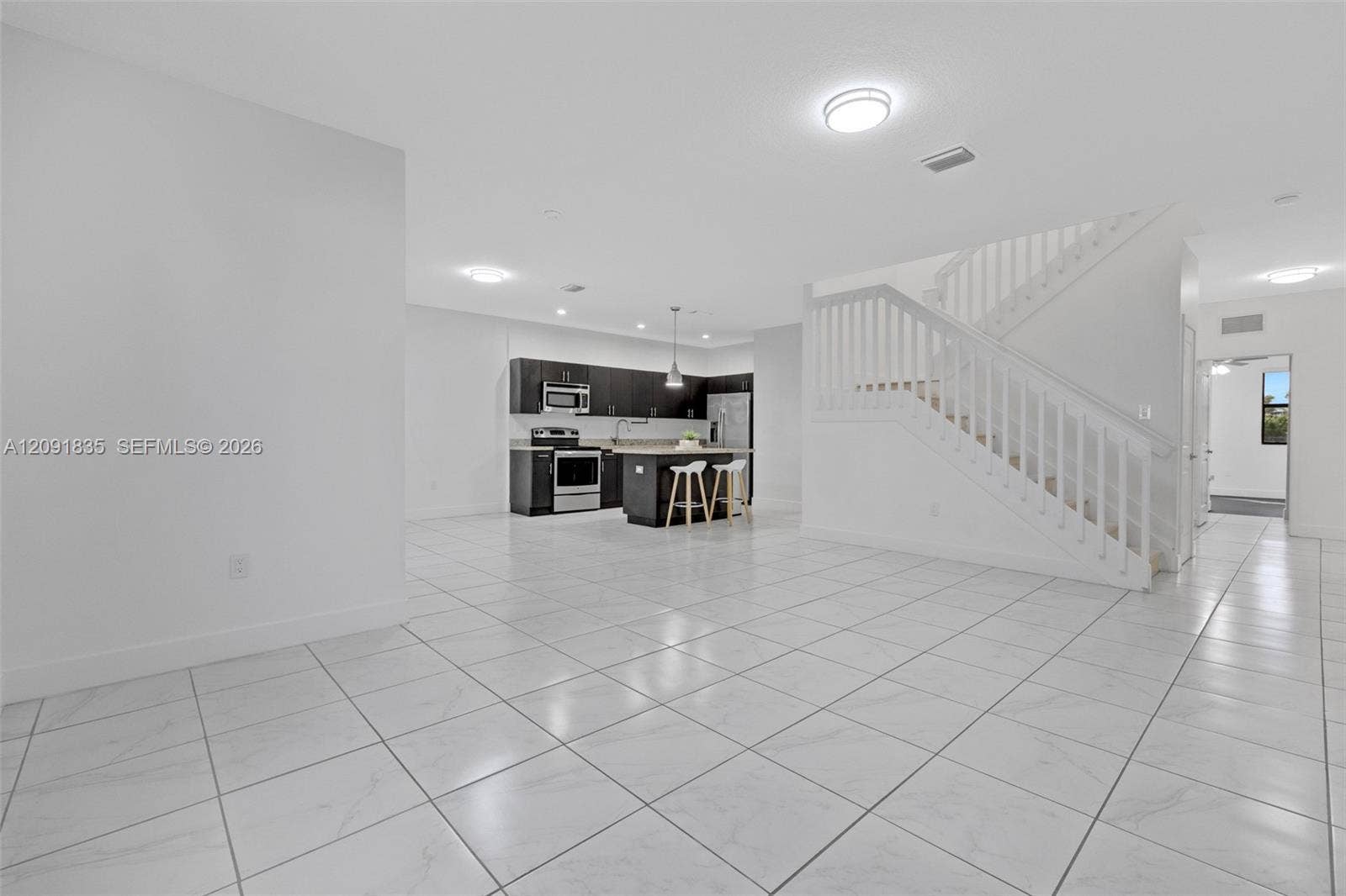 22409 SW 102nd Avenue, Miami, FL 33190 Open-concept interior featuring light-toned tile flooring, kitchen with dark cabinetry, central island, and staircase with white railings