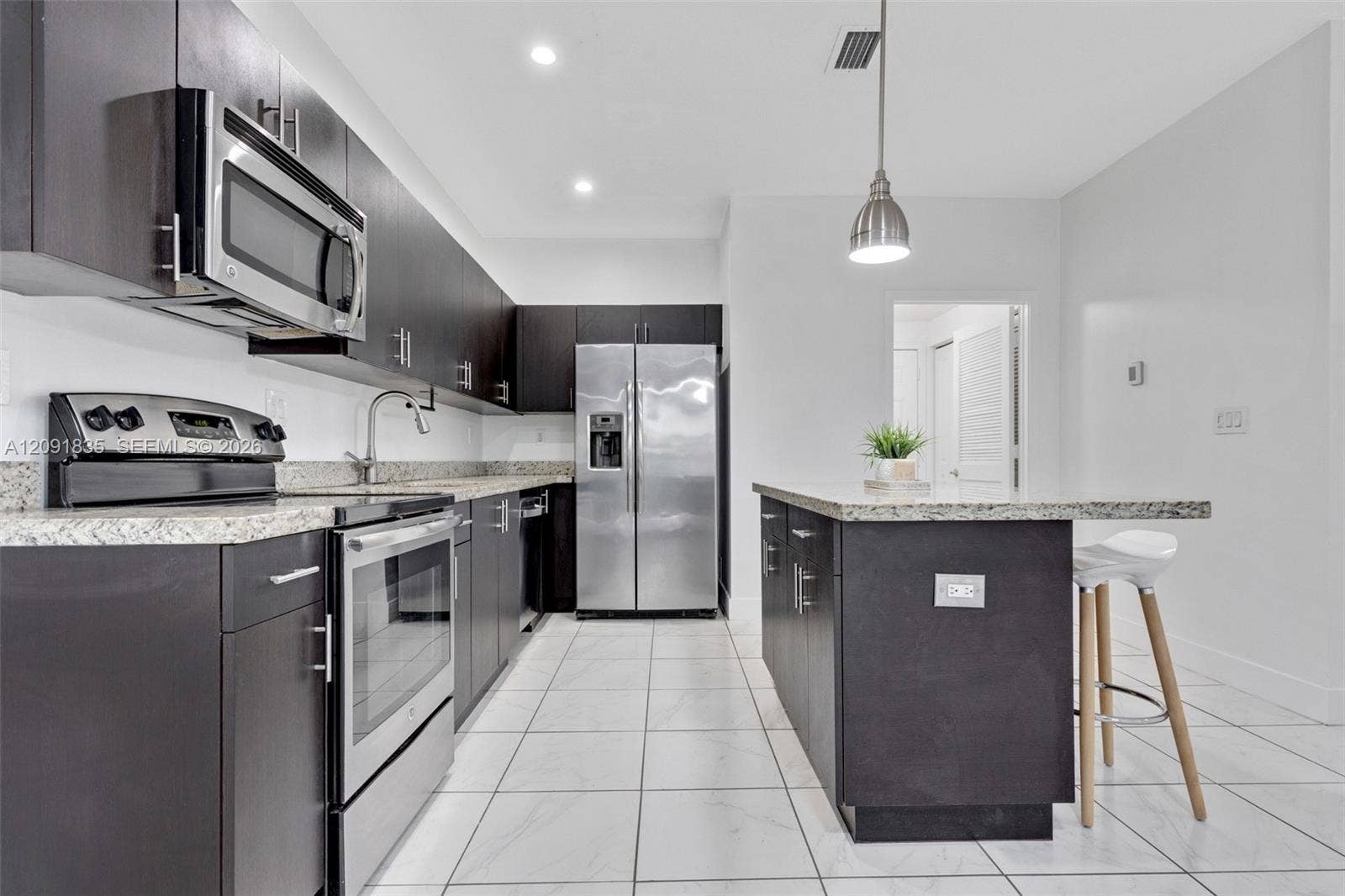 22409 SW 102nd Avenue, Miami, FL 33190 Kitchen featuring flat-panel dark cabinetry, speckled stone-finish countertops, stainless steel appliances, a center island with pendant lighting, and ceramic tile flooring