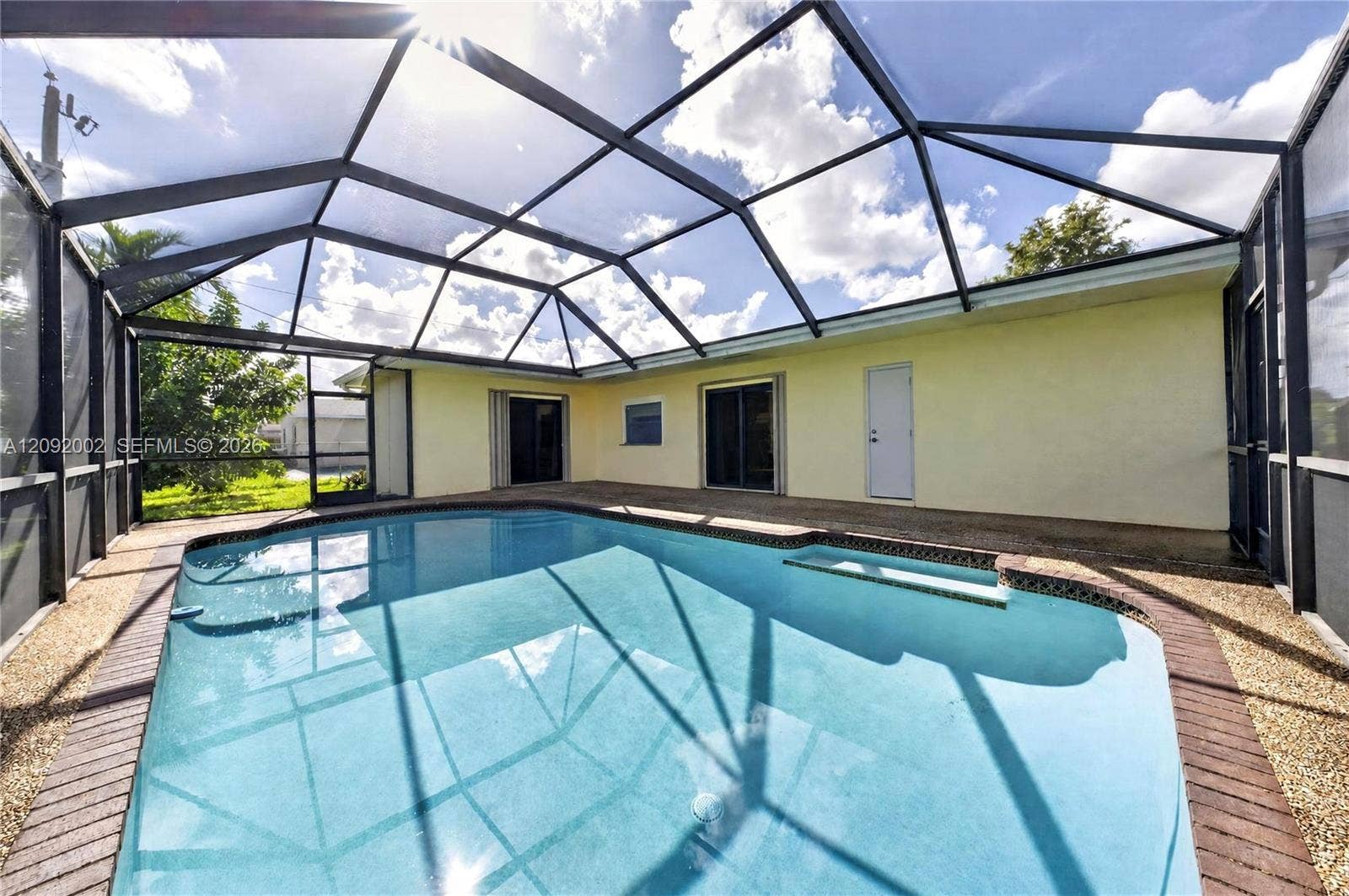 Screened-in patio enclosure featuring an inground swimming pool with a built-in bench and a textured concrete deck