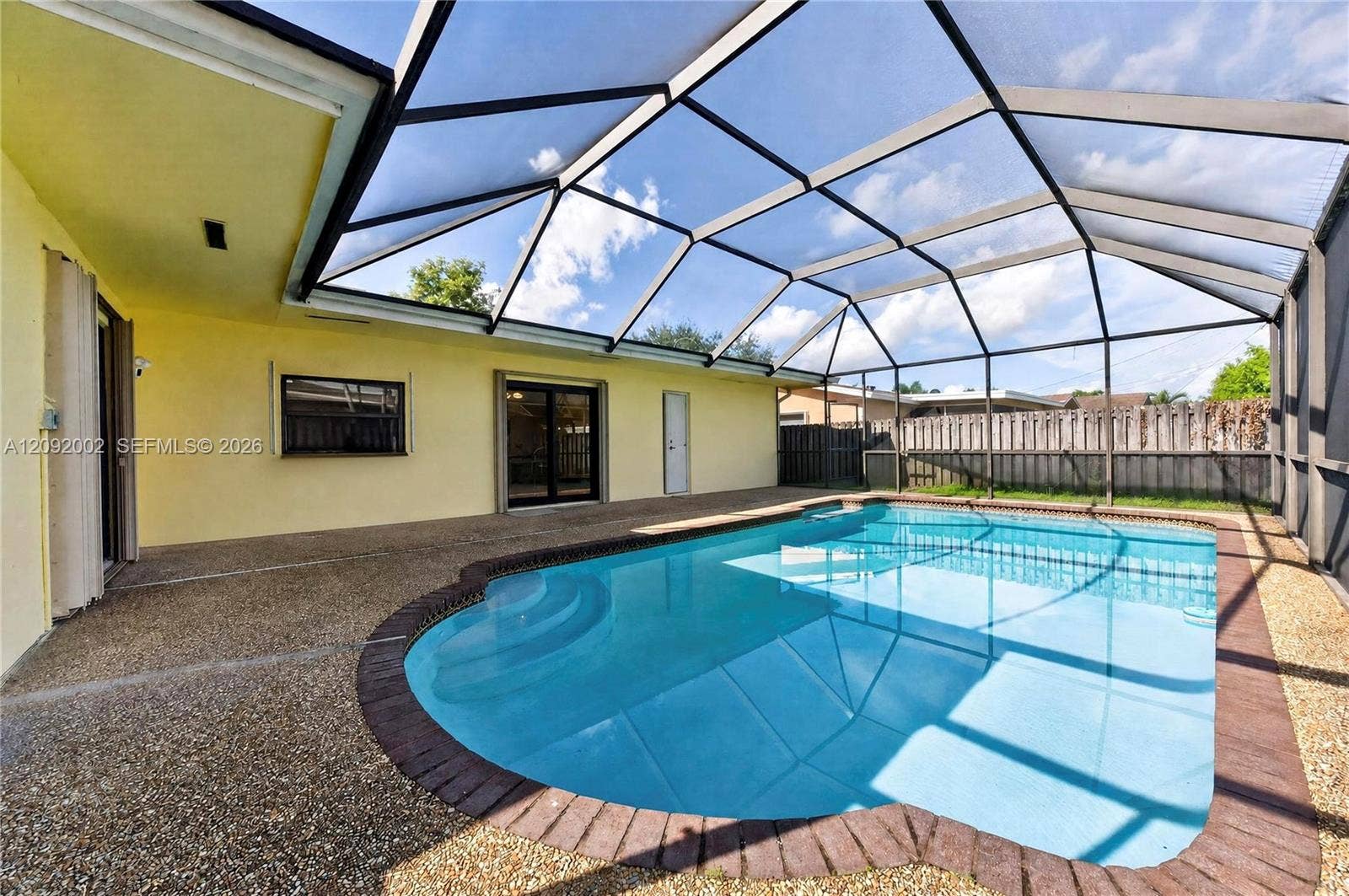 Screened enclosure featuring a swimming pool with integrated steps, textured concrete decking, and a brick paver border