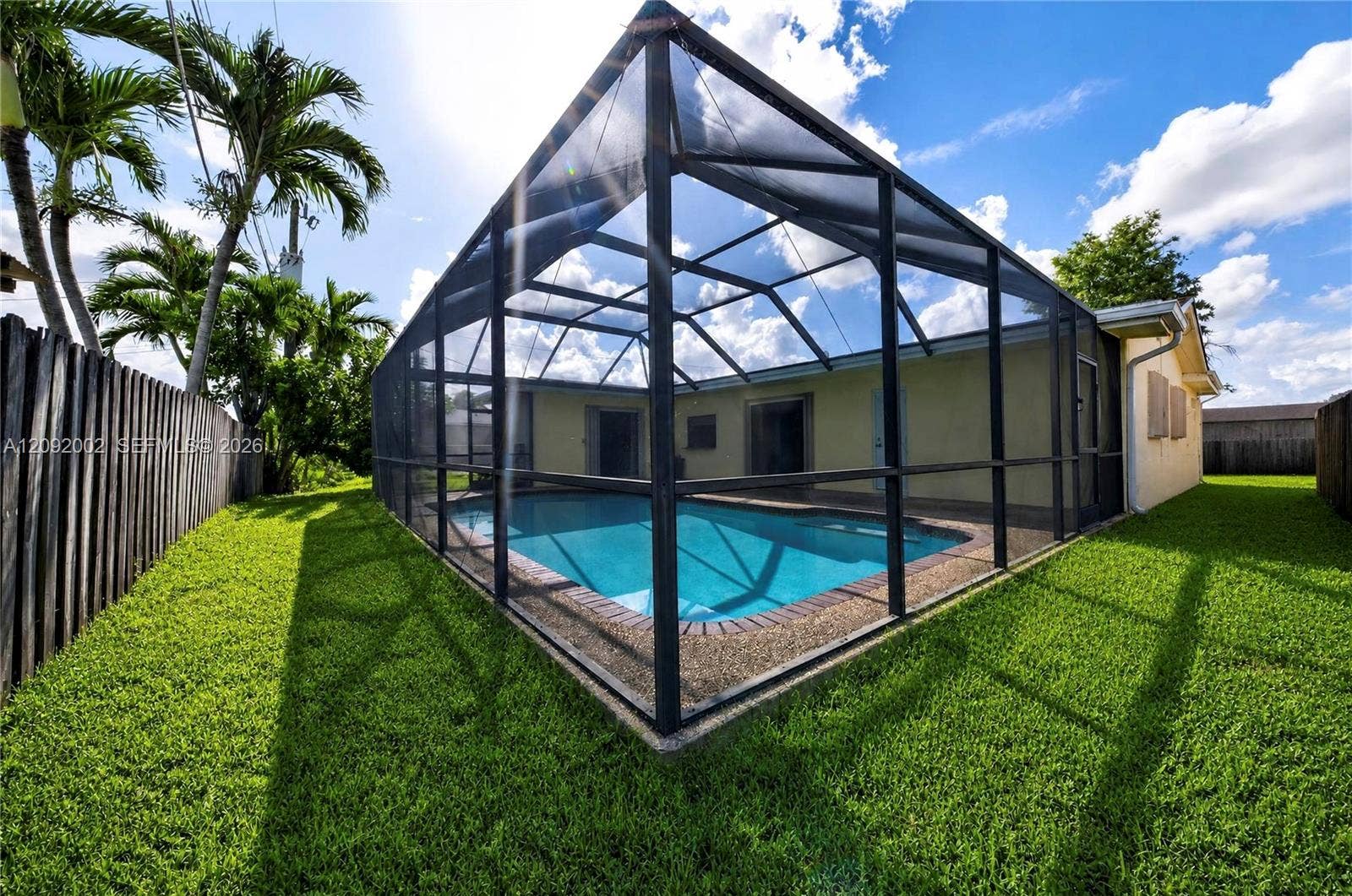 In-ground swimming pool enclosed by a screen structure, featuring a concrete pool deck and a manicured lawn