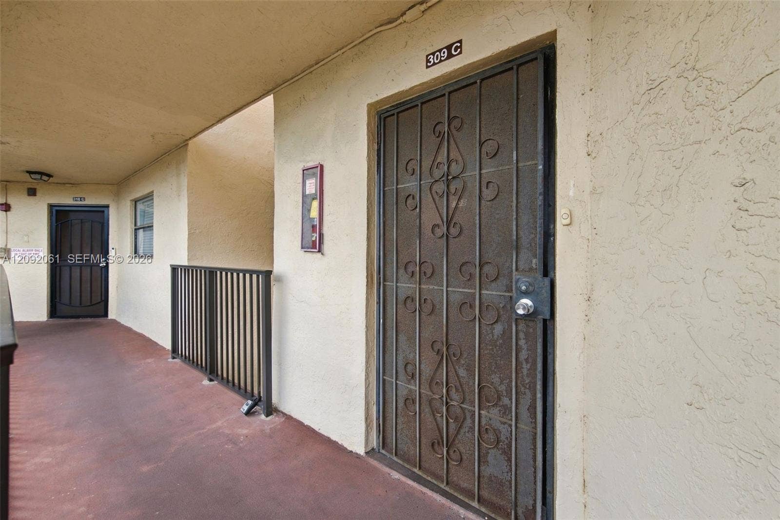 6555 W Broward Boulevard, #309, Plantation, FL 33317 Covered exterior walkway featuring a metal security screen door with decorative scrollwork and a vertical metal balustrade