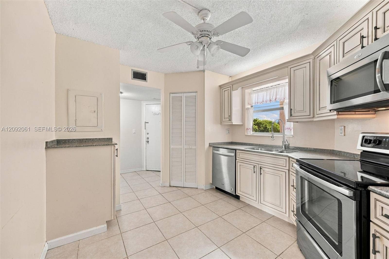 6555 W Broward Boulevard, #309, Plantation, FL 33317 Kitchen featuring light-toned cabinetry, stainless steel appliances, neutral stone-finish countertops, ceramic tile flooring, and a ceiling fan