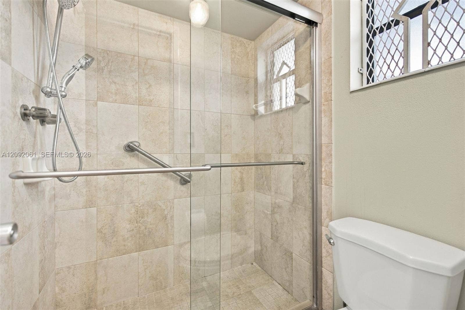 6555 W Broward Boulevard, #309, Plantation, FL 33317 Walk-in shower enclosure with glass sliding doors, stone-finish tile surround, handheld shower fixture, and wall-mounted metal grab bar