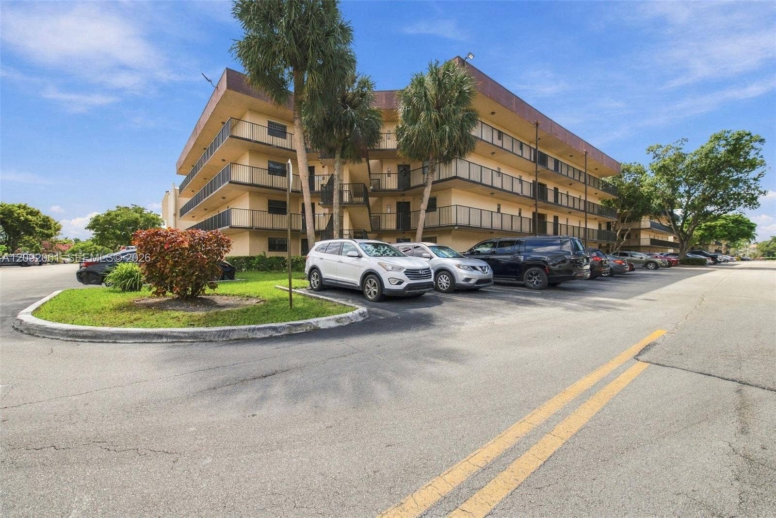 6555 W Broward Boulevard, #309, Plantation, FL 33317 Multi-story residential building exterior featuring private balconies with metal railings, mature palm trees, and asphalt surface parking