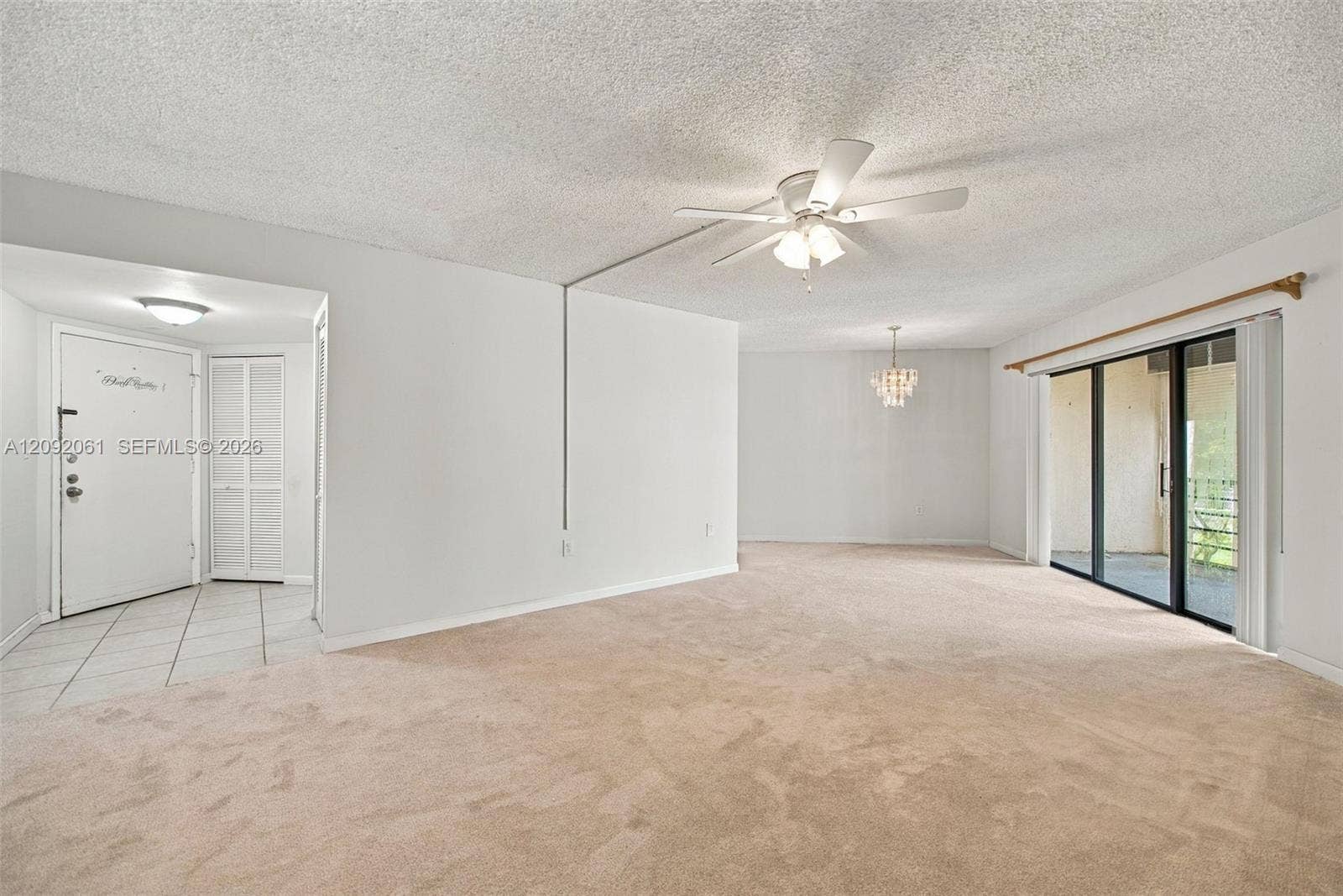 6555 W Broward Boulevard, #309, Plantation, FL 33317 Open-concept interior featuring wall-to-wall carpeting, a ceiling fan with integrated lighting, a multi-pane glass sliding door, and a tiled entryway with louvered-door closet