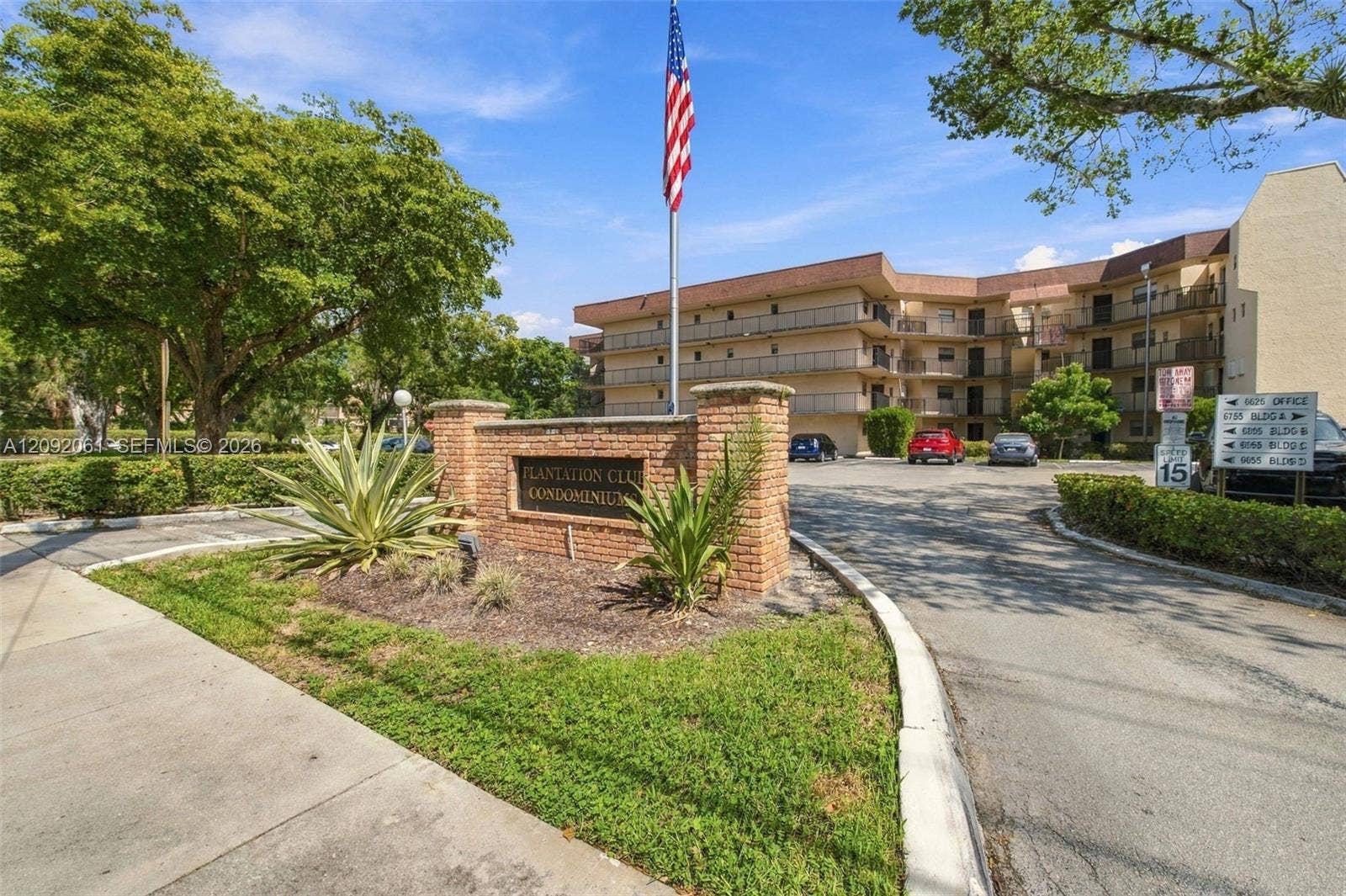 6555 W Broward Boulevard, #309, Plantation, FL 33317 Community entrance featuring a brick monument sign, mature landscaping, and asphalt driveway
