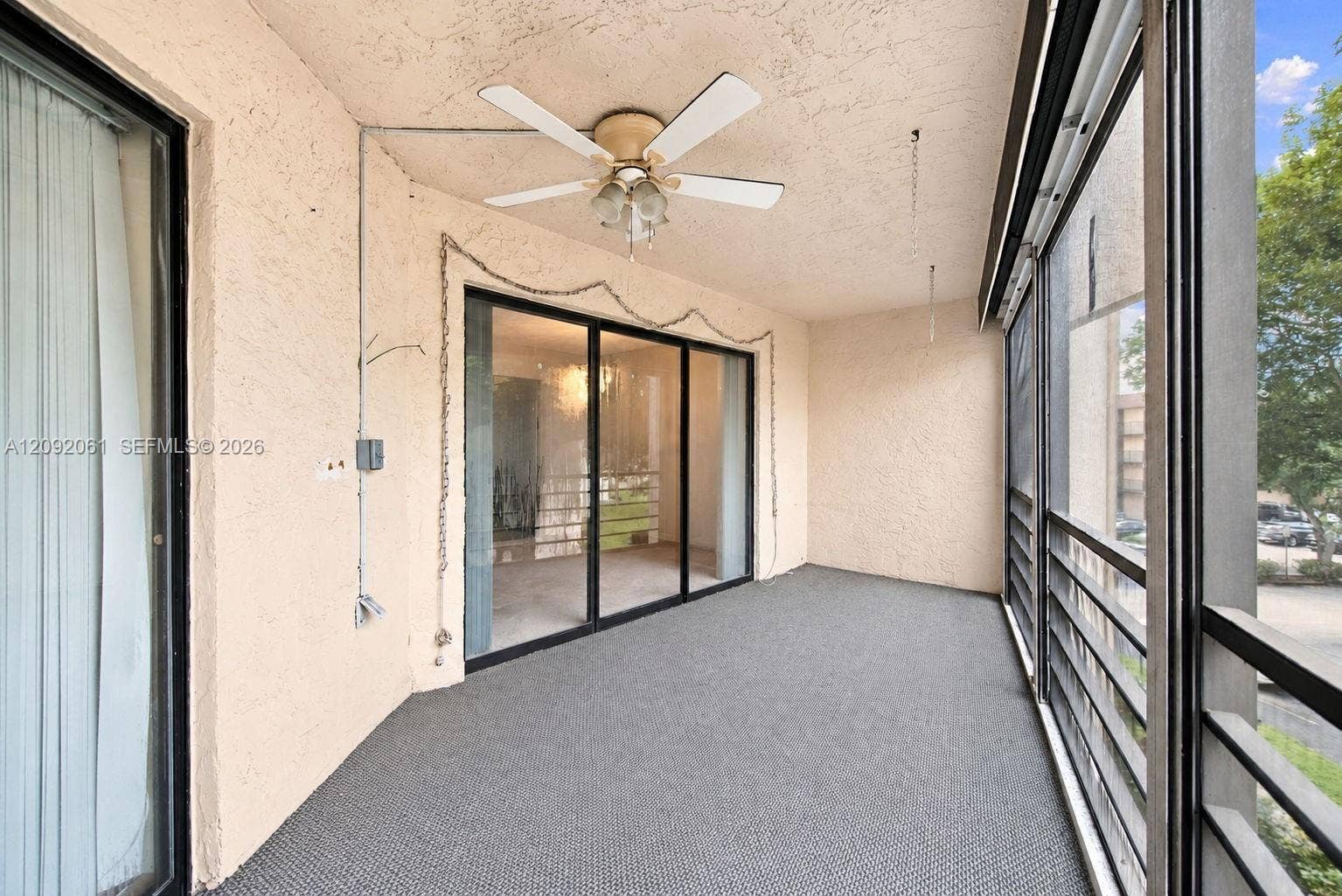 6555 W Broward Boulevard, #309, Plantation, FL 33317 Screened-in balcony featuring stucco walls, a ceiling fan with integrated lighting, metal railings, and sliding glass entry doors