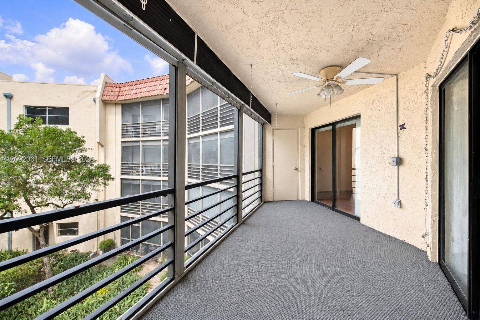 6555 W Broward Boulevard, #309, Plantation, FL 33317 Screened balcony featuring metal railings, textured wall finish, ceiling fan, and carpeted flooring