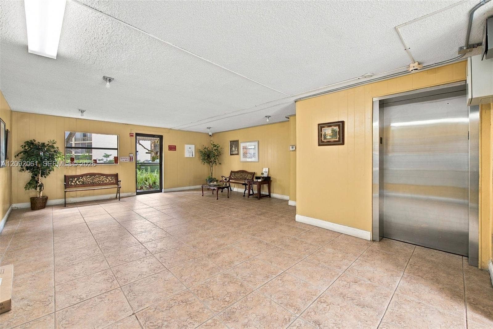 6555 W Broward Boulevard, #309, Plantation, FL 33317 Common area lobby featuring tile flooring, panel-accented walls, and a stainless steel elevator