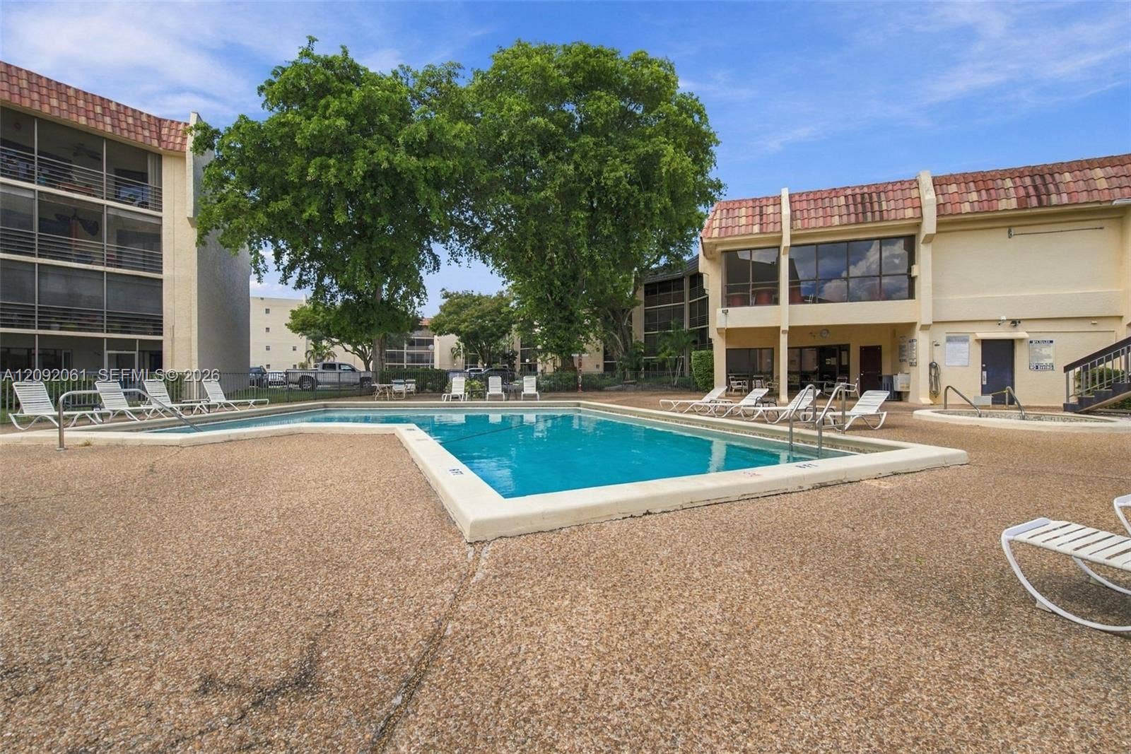 6555 W Broward Boulevard, #309, Plantation, FL 33317 Community swimming pool featuring a textured concrete deck, tile roof architecture, and mature trees