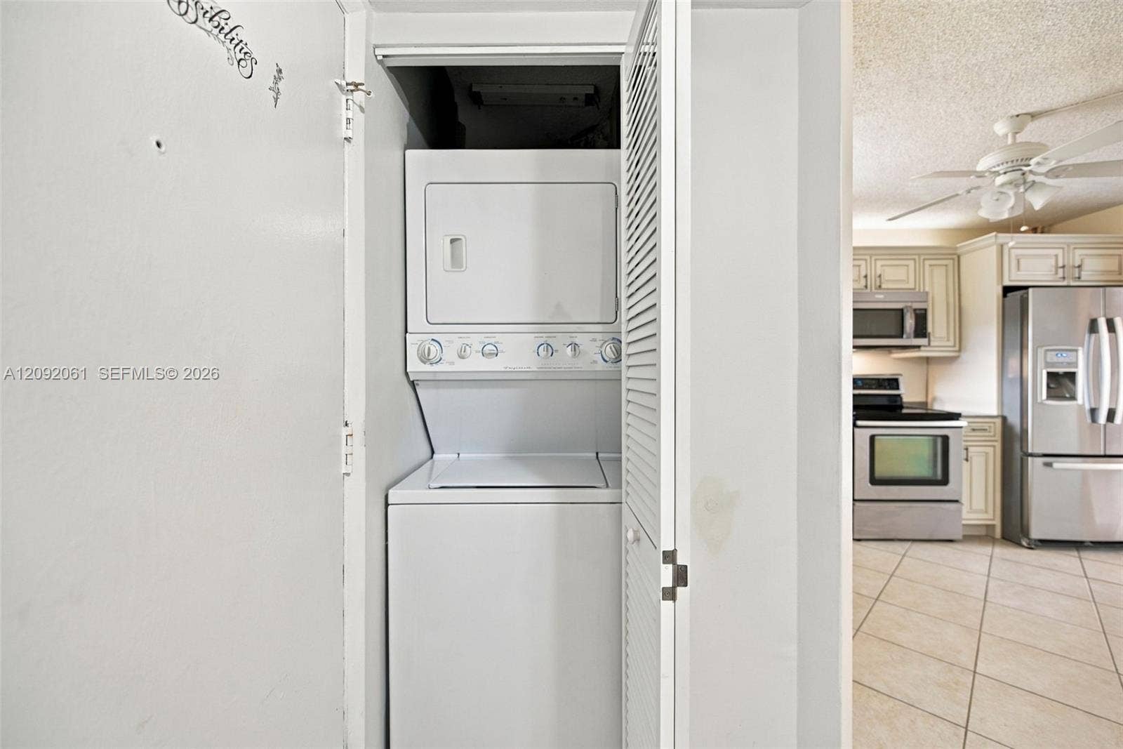 6555 W Broward Boulevard, #309, Plantation, FL 33317 Laundry closet featuring a stackable washer and dryer, louvered bi-fold door, and kitchen area with stainless steel appliances, cabinetry, and tile flooring