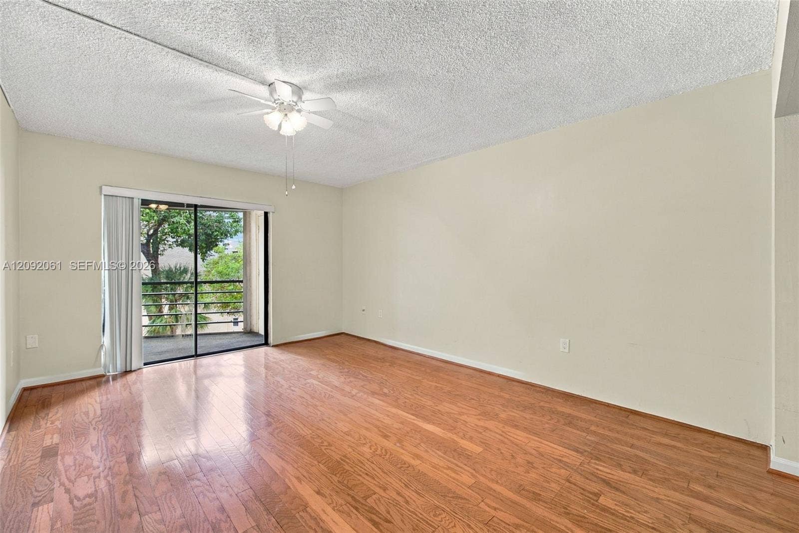 6555 W Broward Boulevard, #309, Plantation, FL 33317 Interior space featuring wood-finish flooring, textured ceiling, ceiling fan with light fixture, and sliding glass door with access to a railed balcony