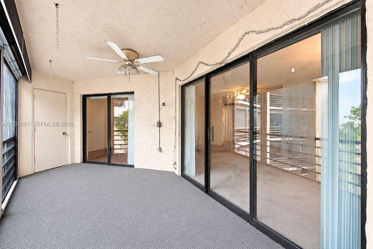 6555 W Broward Boulevard, #309, Plantation, FL 33317 Covered balcony featuring dual sliding glass door entries, textured walls, wall-to-wall carpeting, and a ceiling-mounted fan with integrated light fixture