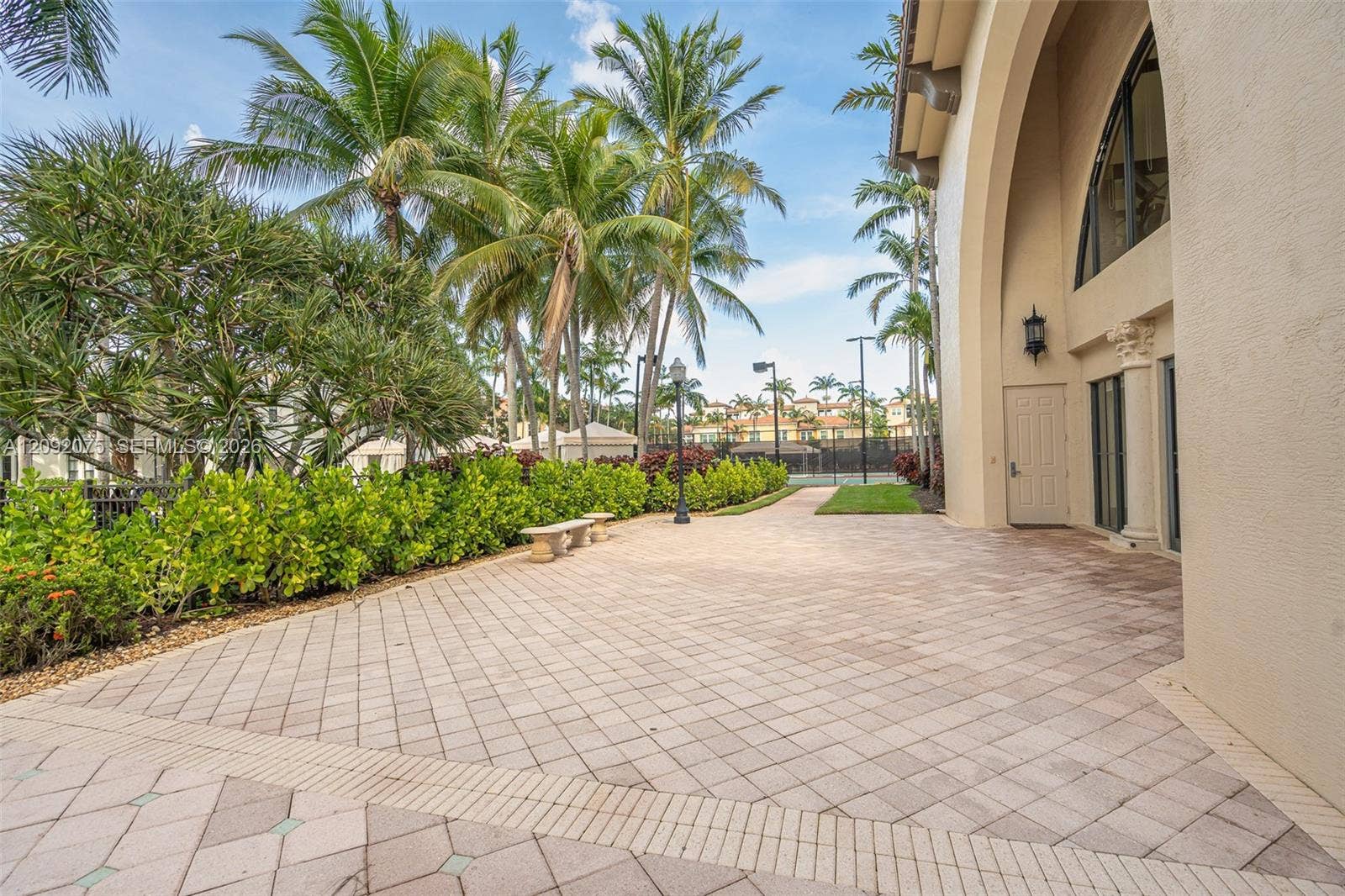 3055 NW 126th Avenue, #219, Sunrise, FL 33323 Expansive paver patio with a decorative border, surrounded by lush landscaping and mature palm trees