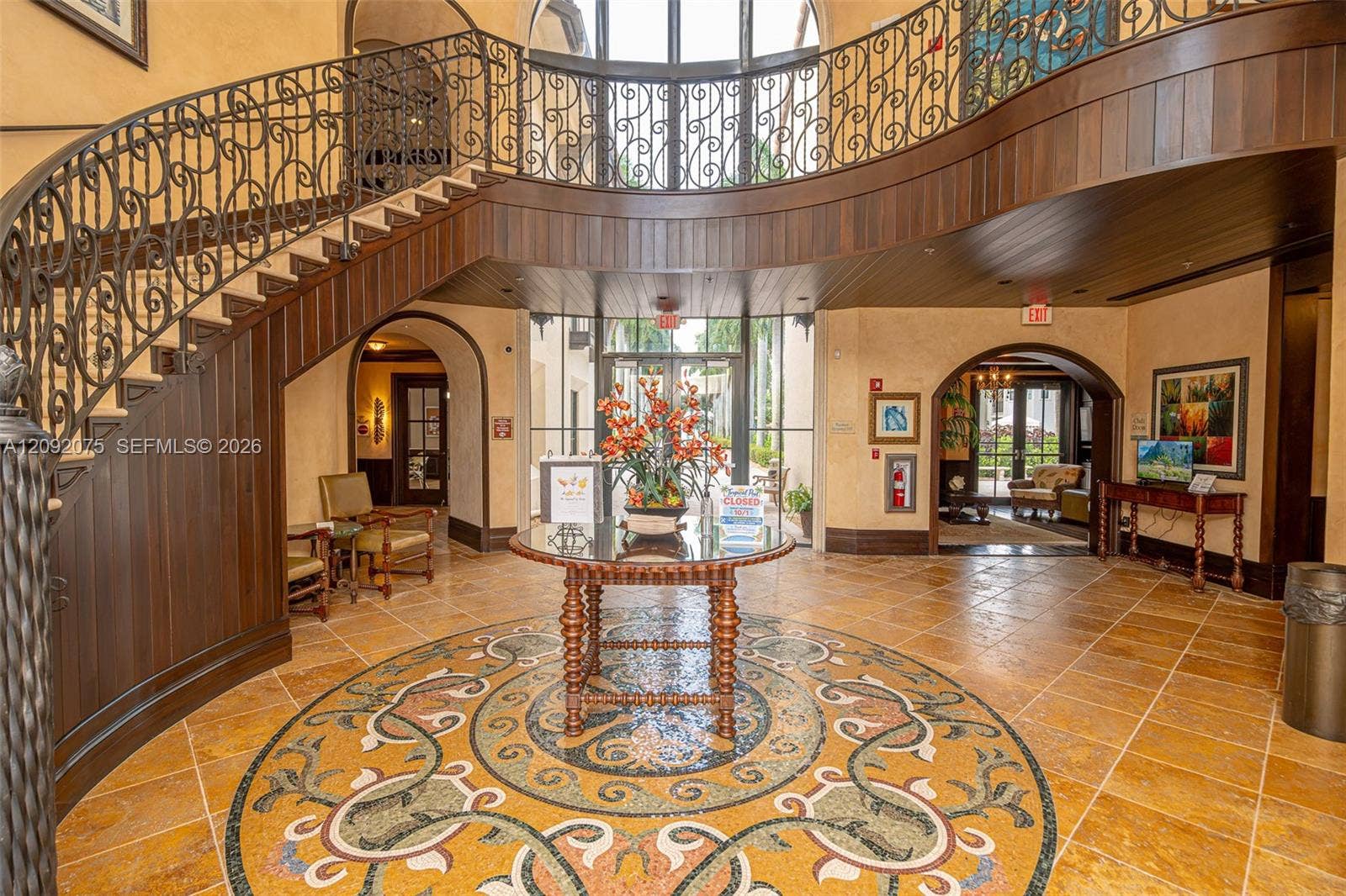 3055 NW 126th Avenue, #219, Sunrise, FL 33323 Grand foyer with a curved staircase featuring wrought iron railings, wood paneling, a detailed mosaic floor medallion, and arched doorways