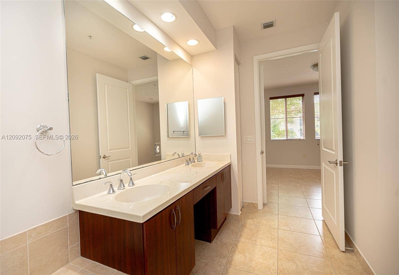3055 NW 126th Avenue, #219, Sunrise, FL 33323 Dual vanity with integrated sinks, expansive mirror, wood-finish cabinetry, and tiled flooring