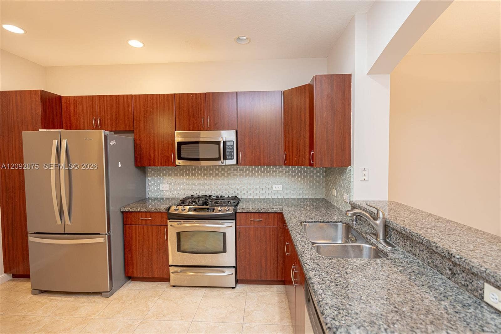 3055 NW 126th Avenue, #219, Sunrise, FL 33323 Kitchen featuring wood-finish cabinetry, stainless steel appliances, a tile backsplash, and granite countertops