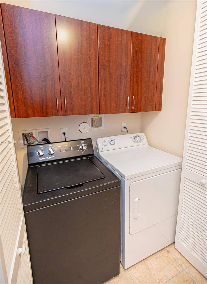 3055 NW 126th Avenue, #219, Sunrise, FL 33323 Wood-finish upper cabinetry with brushed nickel hardware, a black top-load washer, and a white front-load dryer