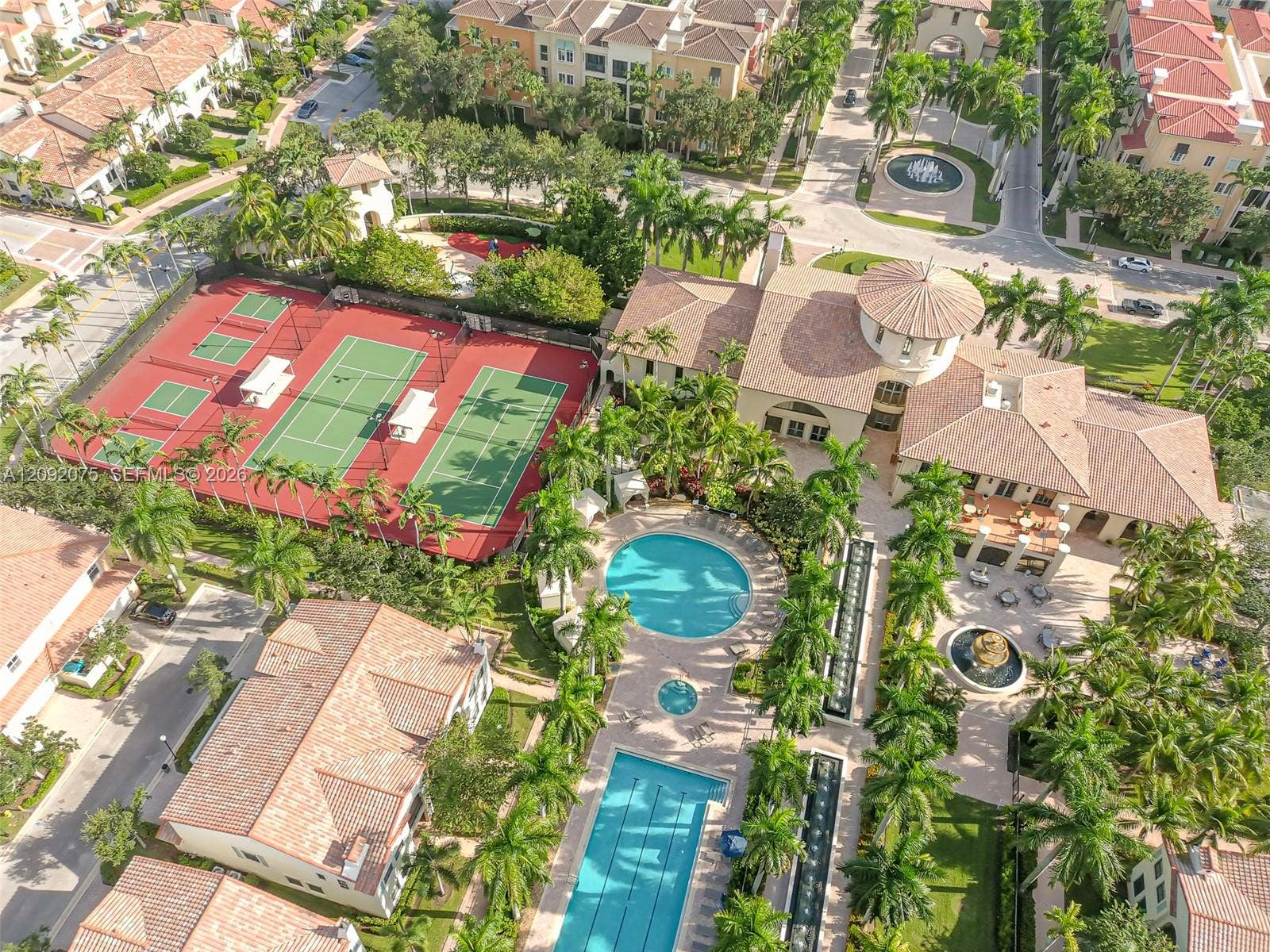 3055 NW 126th Avenue, #219, Sunrise, FL 33323 Community amenities featuring multiple tennis courts, a circular swimming pool, a rectangular swimming pool, a central clubhouse building, and mature palm tree landscaping