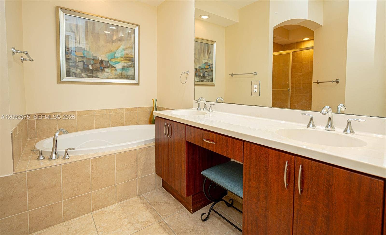 3055 NW 126th Avenue, #219, Sunrise, FL 33323 Double vanity with integrated sinks, wood-finish cabinetry, a large mirror, and a built-in soaking tub with tiled surround
