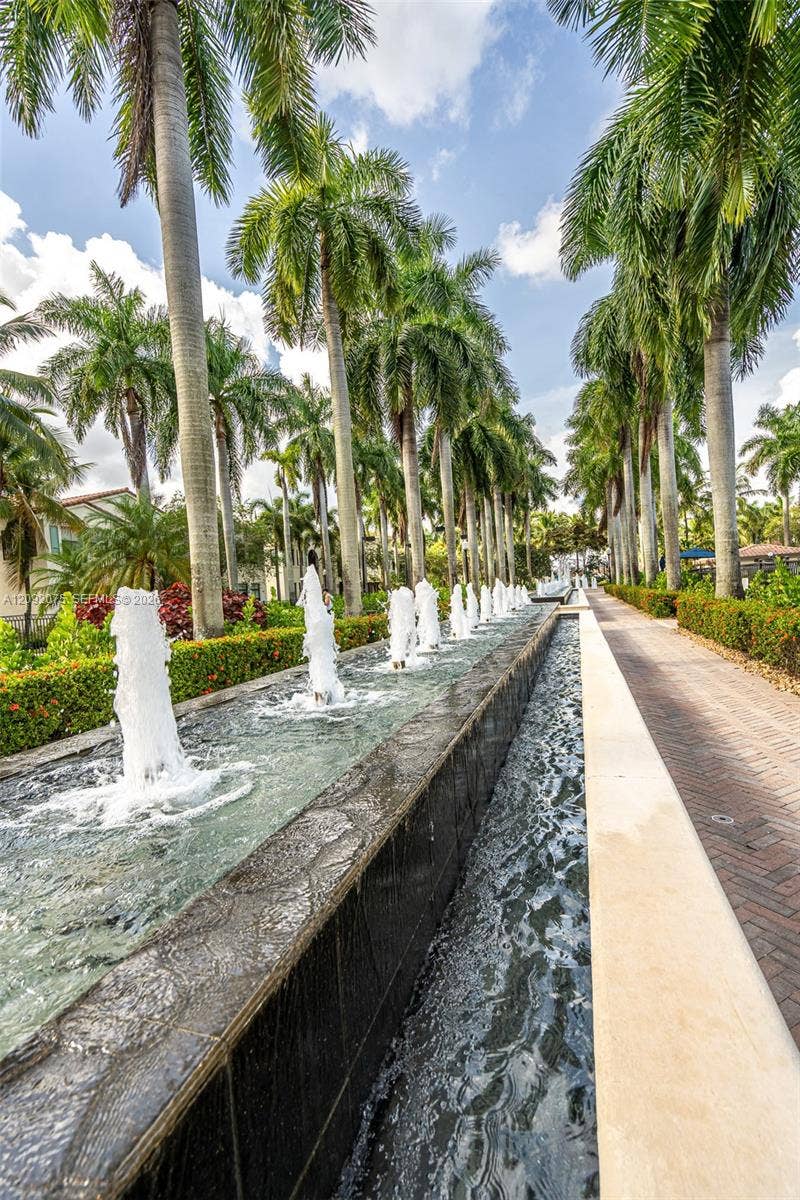 3055 NW 126th Avenue, #219, Sunrise, FL 33323 Water feature with multiple fountain jets, flanked by a paved walkway and rows of mature palm trees