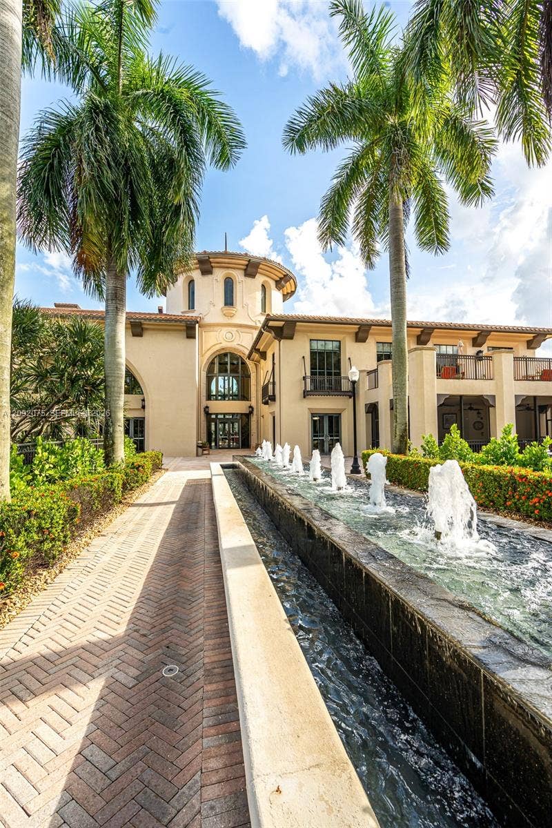 3055 NW 126th Avenue, #219, Sunrise, FL 33323 Stately stucco exterior with a prominent rotunda, a linear water feature with multiple fountains, a herringbone-patterned brick paver walkway, and mature palm trees