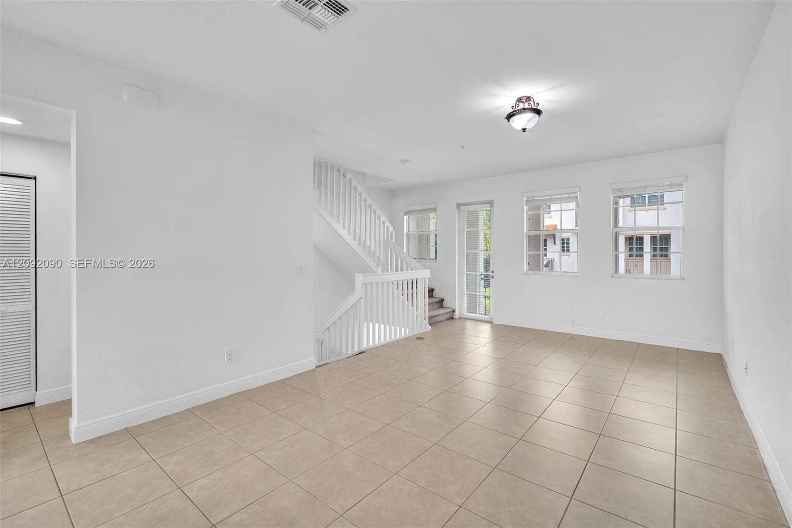 11979 SW 28th Court, Miramar, Miramar, FL 33025 Open-concept interior featuring large-format ceramic tile flooring, a white wooden staircase with balustrades, multiple grid-pane windows, and a glass-paneled exterior door