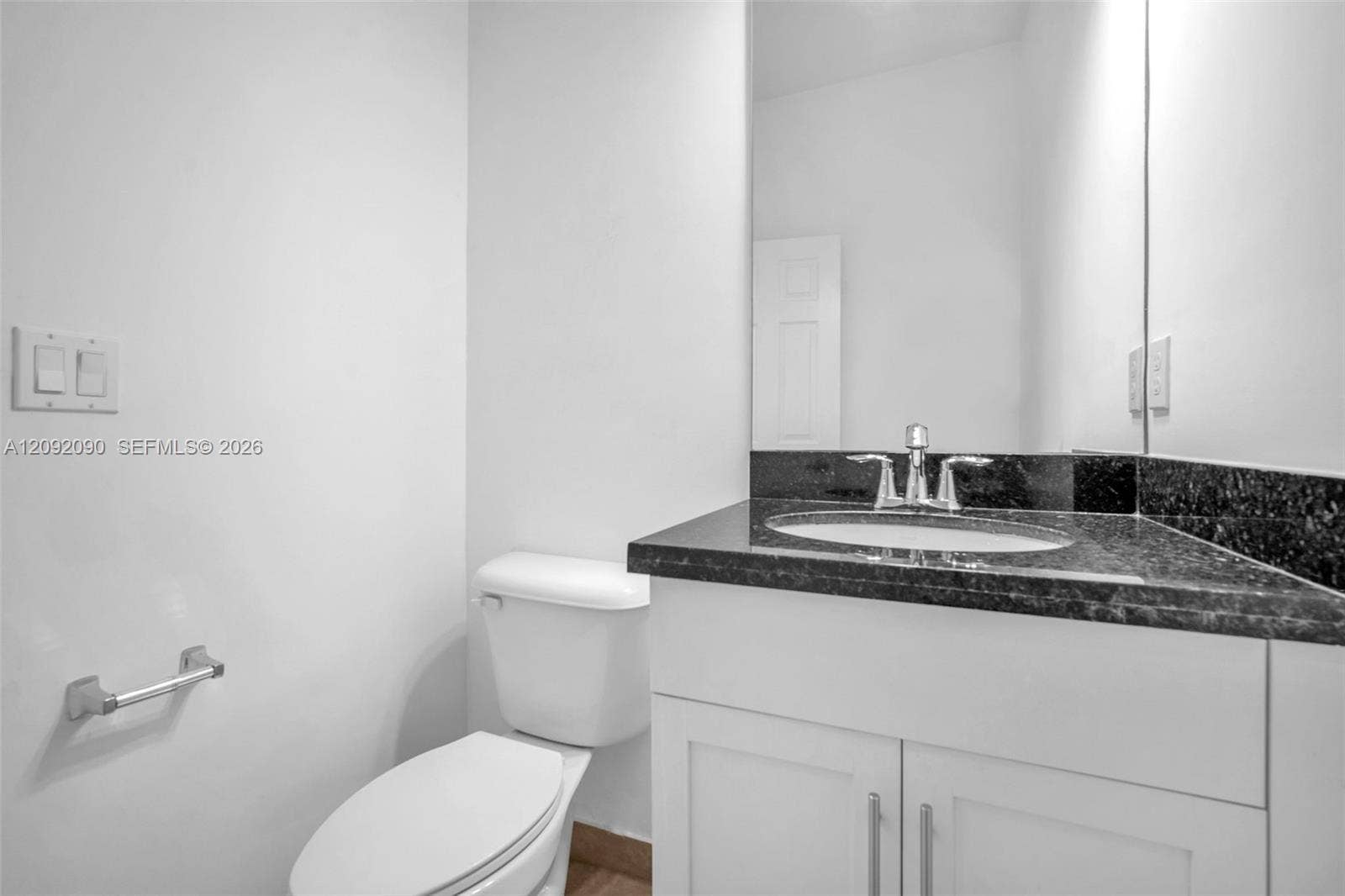 11979 SW 28th Court, Miramar, Miramar, FL 33025 Vanity featuring a dark stone countertop, integrated oval basin, white shaker-style cabinetry, and polished chrome hardware, complemented by a large wall-mounted mirror
