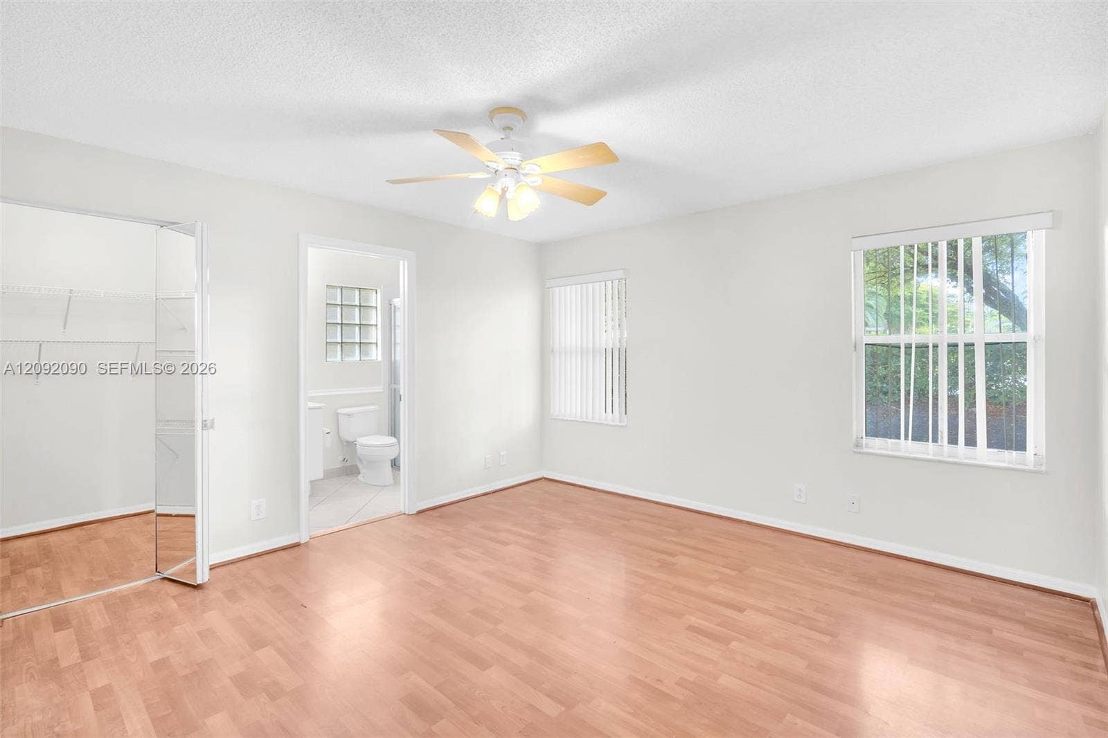 11979 SW 28th Court, Miramar, Miramar, FL 33025 Room featuring wood-finish flooring, a ceiling fan with integrated lighting, dual windows with vertical blinds, and a built-in walk-in closet with mirrored door panels
