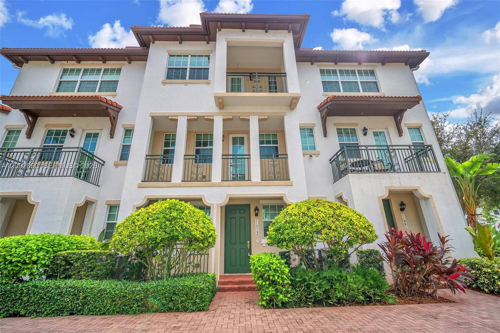 11979 SW 28th Court, Miramar, Miramar, FL 33025 Stucco multi-story exterior featuring a tile roof, multiple wrought-iron balconies, arched entryway detailing, and brick-paver hardscaping