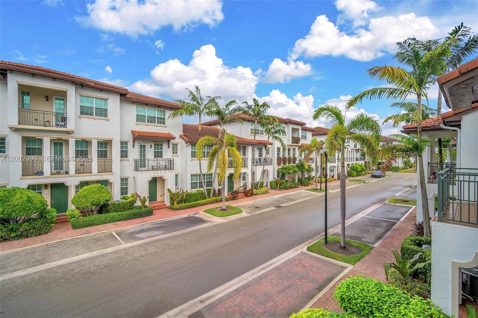 11979 SW 28th Court, Miramar, Miramar, FL 33025 Multi-story stucco townhome exteriors featuring red tile roofing, decorative wrought-iron balconies, private brick-paver walkways, and mature tropical landscaping