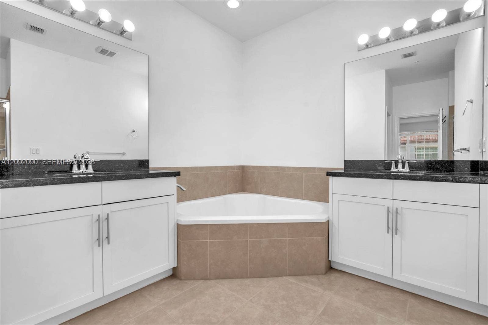 11979 SW 28th Court, Miramar, Miramar, FL 33025 Dual white vanities with dark stone countertops, corner soaking tub with tile surround, two large wall-mounted mirrors, and chrome fixtures