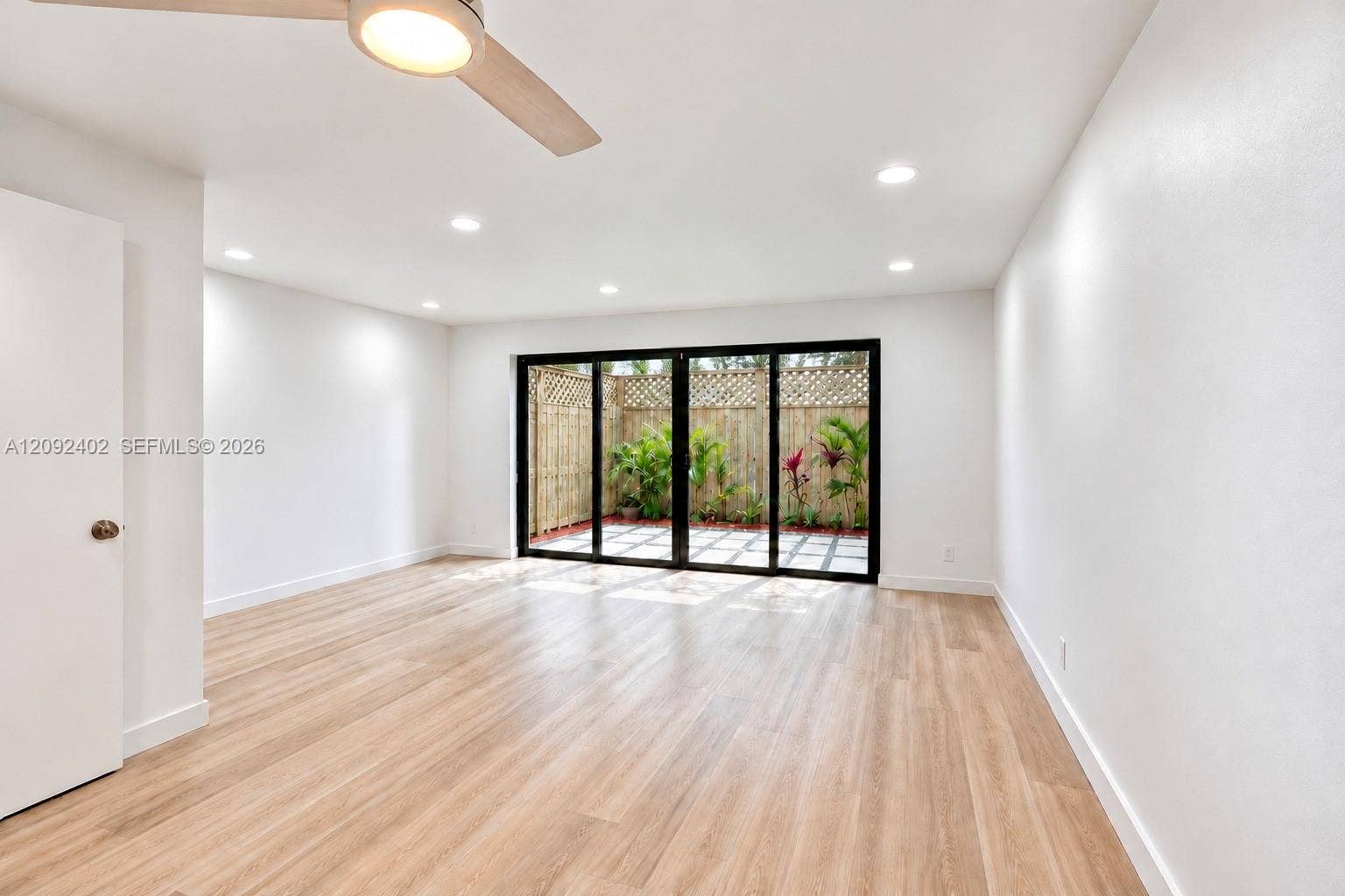 499 SE 13th Street, #7E, Fort Lauderdale, FL 33316 Neutral-toned interior featuring wood-finish flooring, recessed lighting, a modern ceiling fan, and black-framed multi-panel sliding glass doors opening to a fenced patio