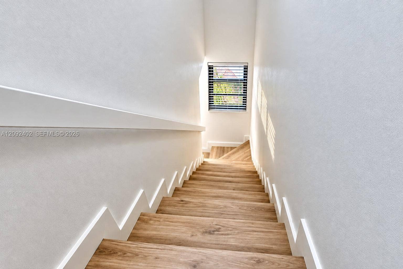 499 SE 13th Street, #7E, Fort Lauderdale, FL 33316 Staircase featuring wood-finish treads, white stringer detailing, a wall-mounted handrail, and a window with horizontal blinds