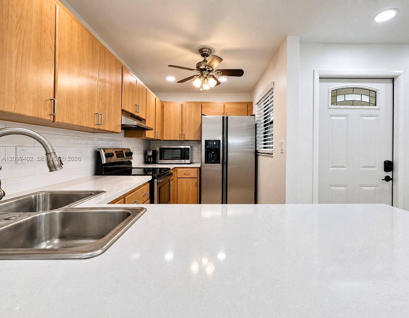 499 SE 13th Street, #7E, Fort Lauderdale, FL 33316 Kitchen featuring light-finish cabinetry, white solid-surface countertops, subway tile backsplash, stainless steel appliances, and a double-basin stainless steel sink